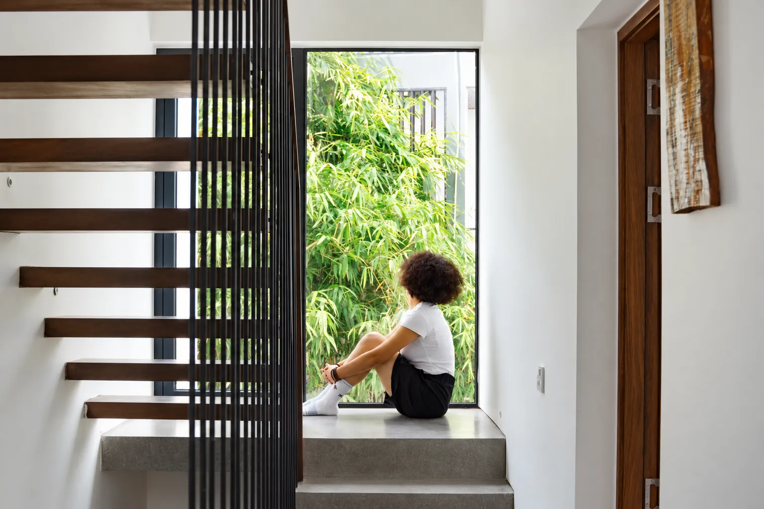 A guest resting by the light-filled staircase and green bamboo at Be-in Home